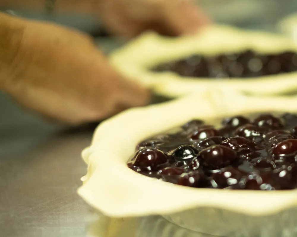 Hands crimping the edge of a berry pie crust in the Boise Pie Co. kitchen