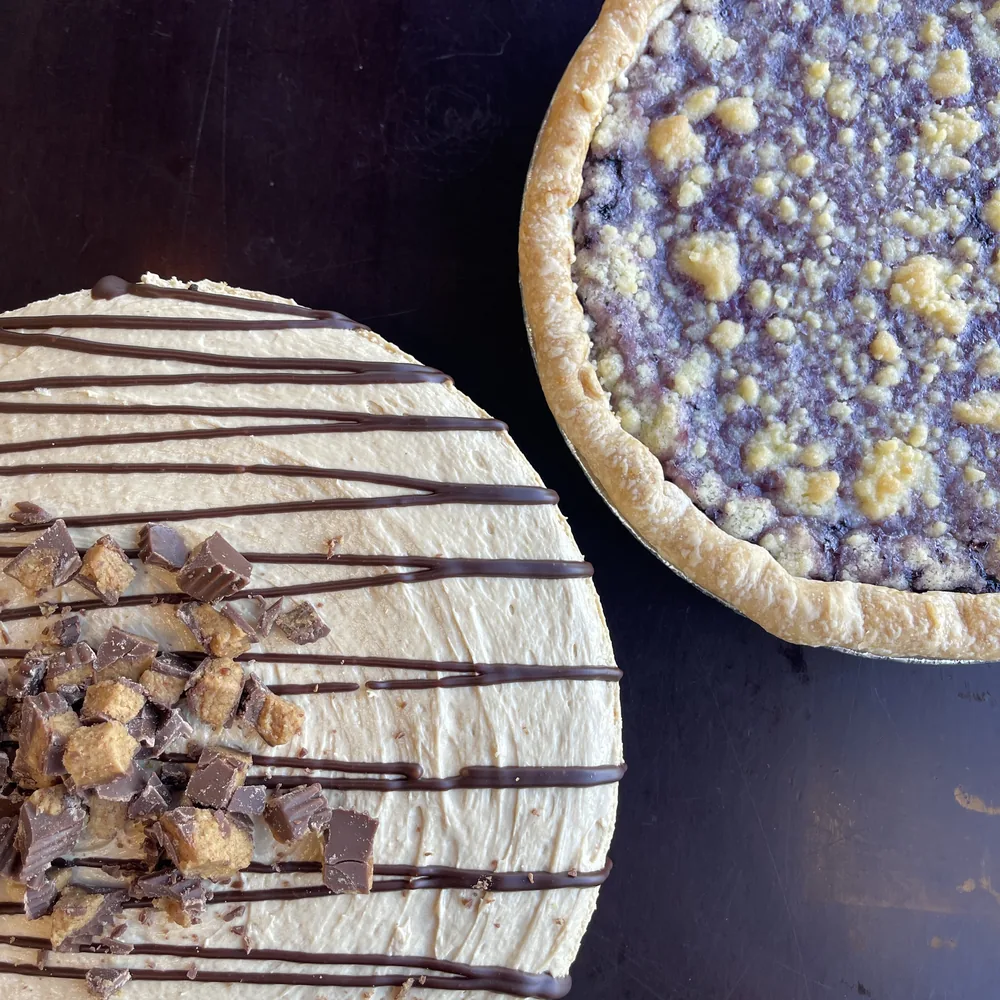 Peanut butter pie with chocolate drizzle and Reese’s next to a blueberry crumble pie at Boise Pie Co. in Boise, Idaho